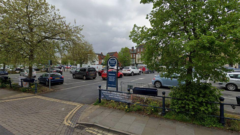 Bargate Green car park in Boston with blue barriers and a blue name sign in the foreground with a number of cars parked in the white marked bays